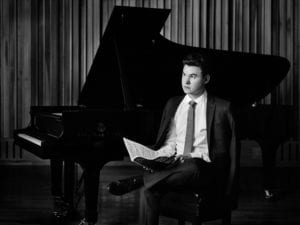 Matthew Graybil sitting next to a piano.